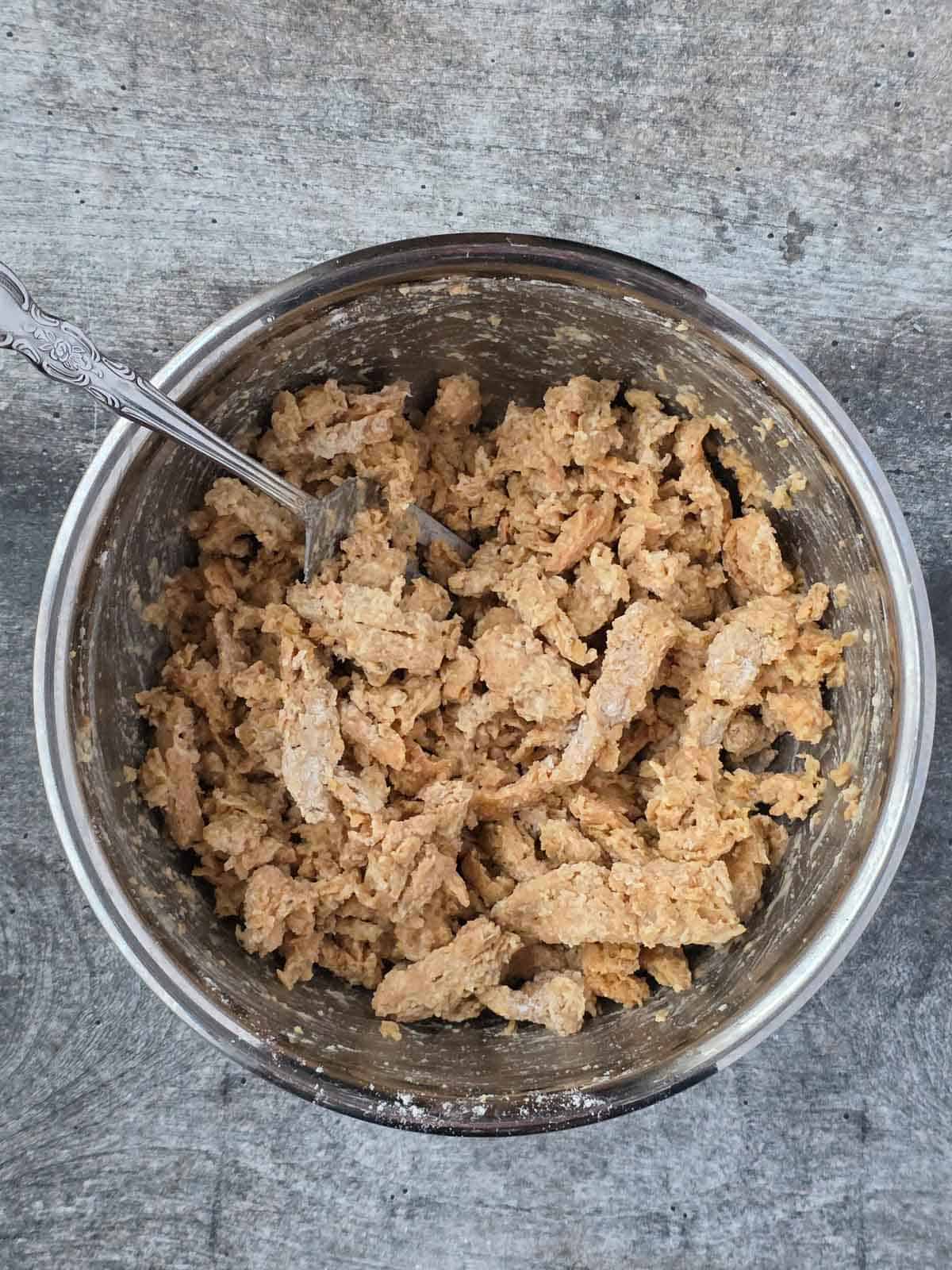 Soy curls coated in seasoned flour inside a mixing bowl, stirred with a fork.