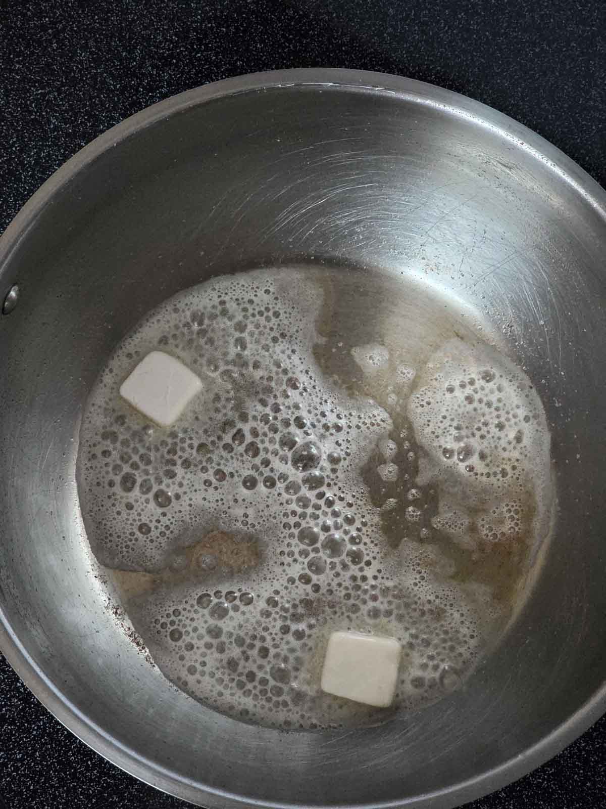 Vegan butter melting and bubbling in a stainless-steel skillet on the stovetop.