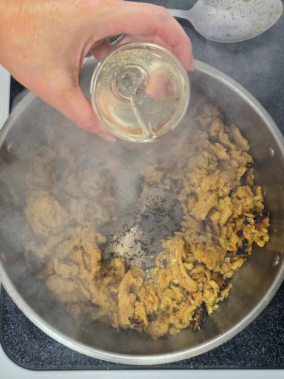 Hand pouring white wine into the skillet to deglaze the browned bits on the bottom.