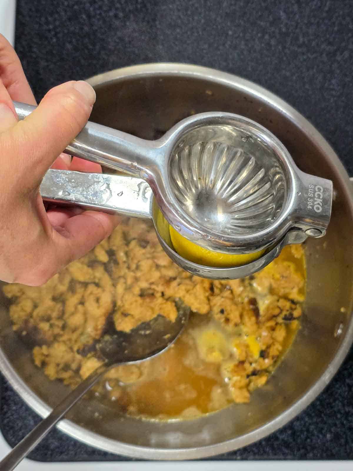 Fresh lemon juice being squeezed into the pan using a handheld metal juicer over the simmering mixture.
