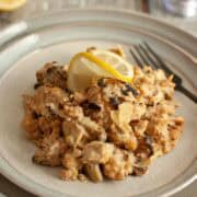 Close-up plate of creamy soy curls with artichokes and capers, topped with a thin lemon slice.
