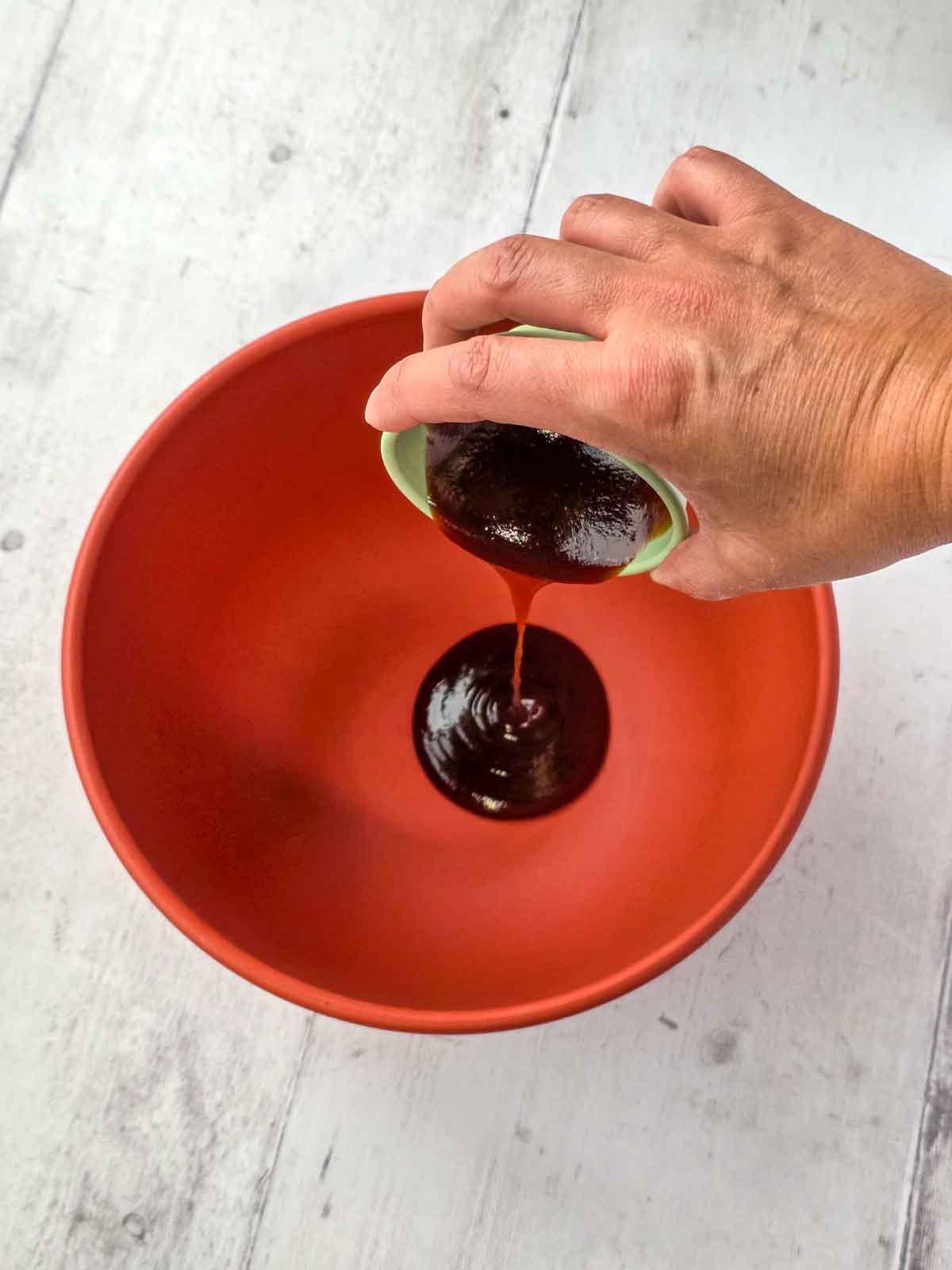 BBQ sauce being poured into a large mixing bowl to start the marinade.