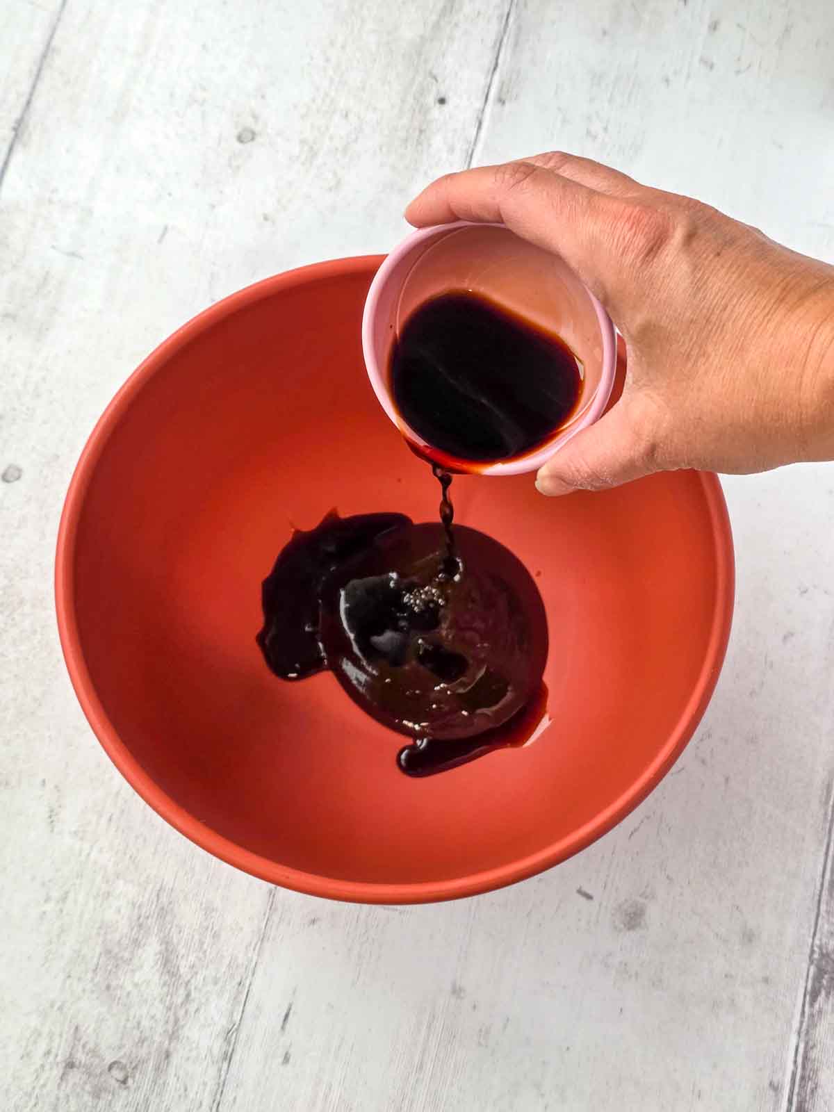 Soy sauce being added to BBQ sauce in a mixing bowl.