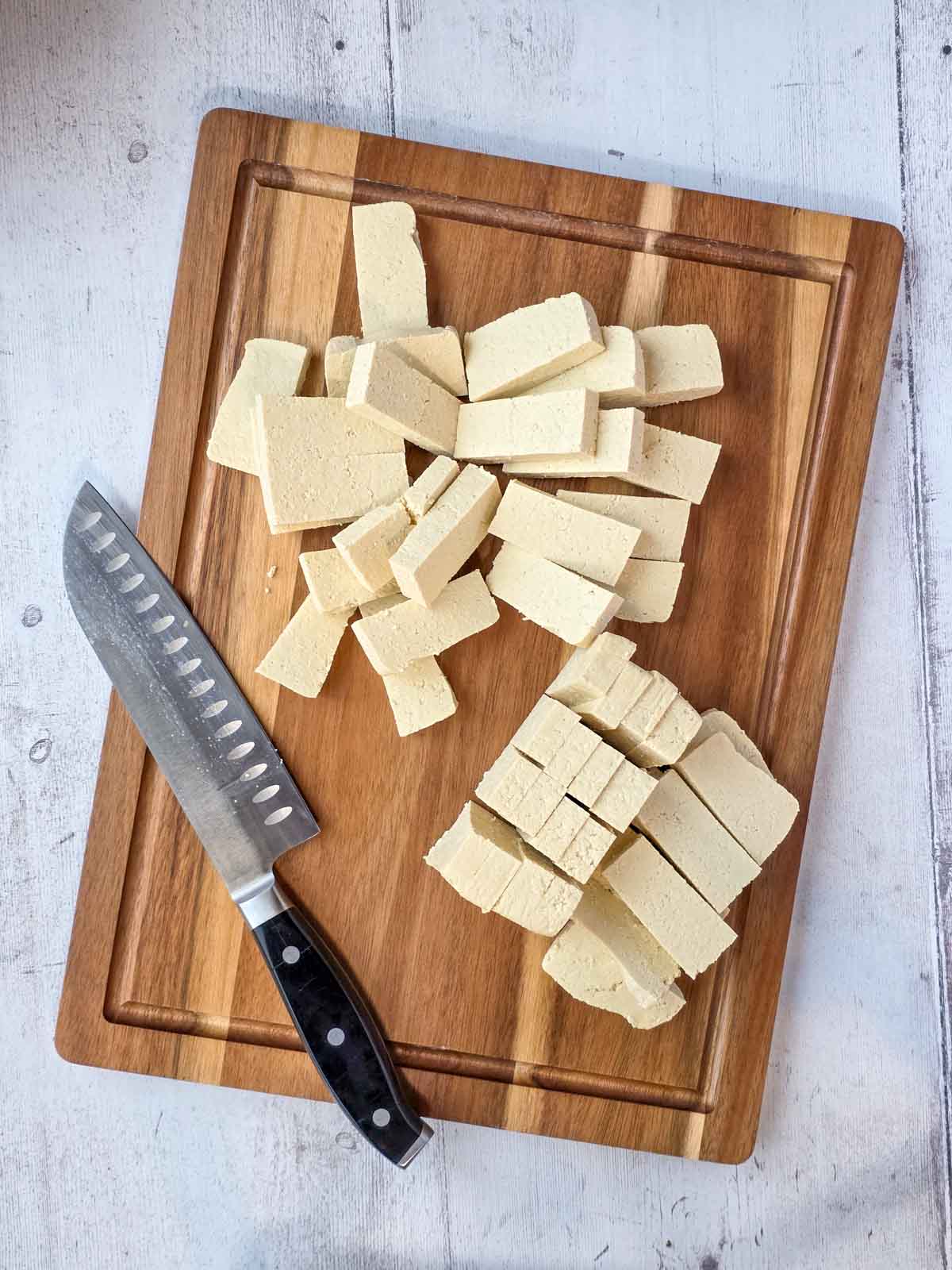 Extra firm vacuum-packed tofu sliced into nugget-sized pieces on a wooden cutting board.