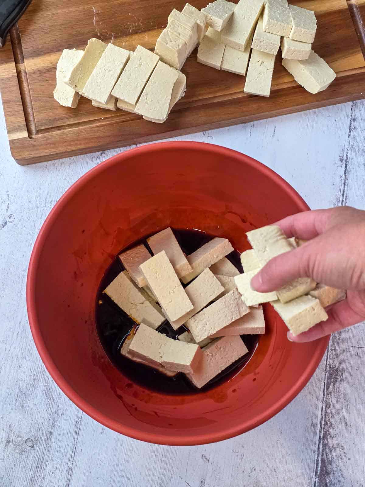 Tofu pieces added to the sauce mixture in a bowl before coating.