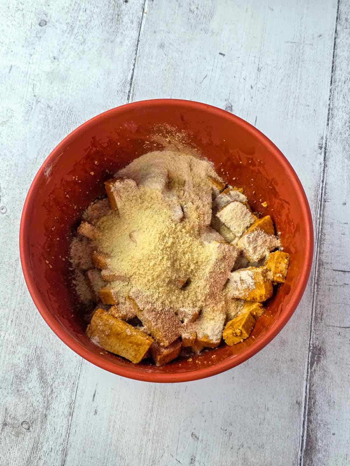 Panko, rice flour, and seasonings added to a large red mixing bowl over top of the tofu pieces.