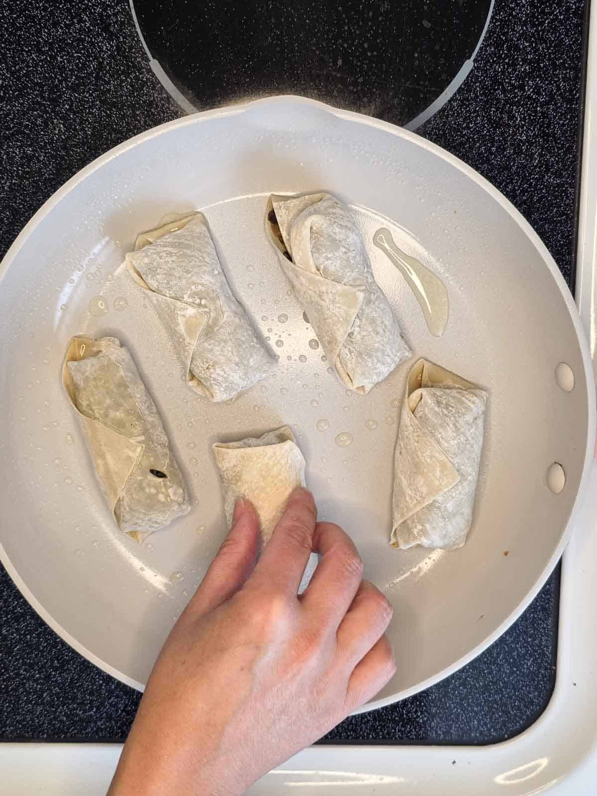 Arranging egg rolls in a skillet so they cook evenly without overcrowding.