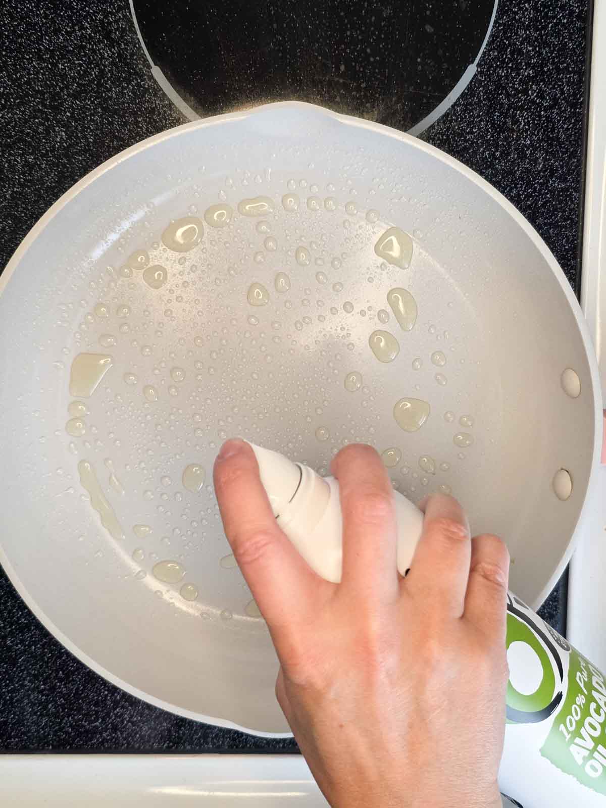 Lightly spraying a nonstick pan with oil before cooking egg rolls.
