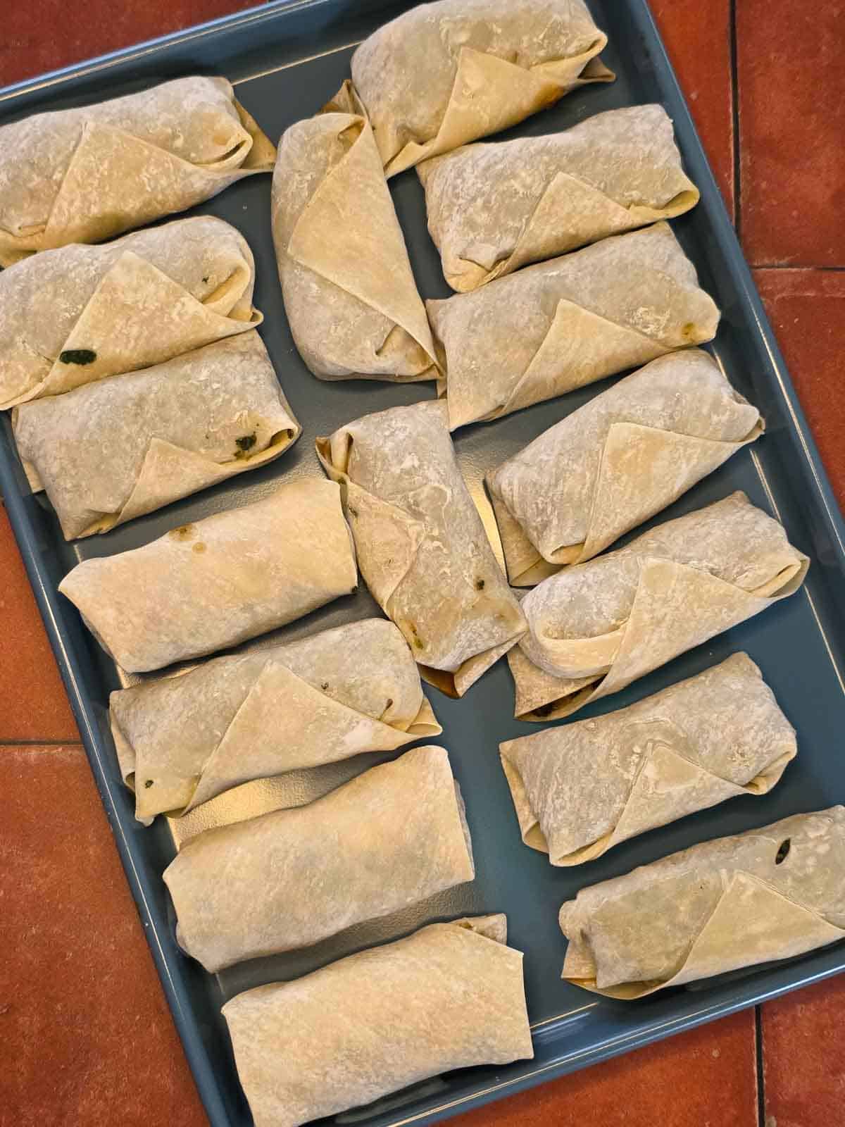 Assembled egg rolls wrapped and ready to be cooked, arranged on a blue tray.