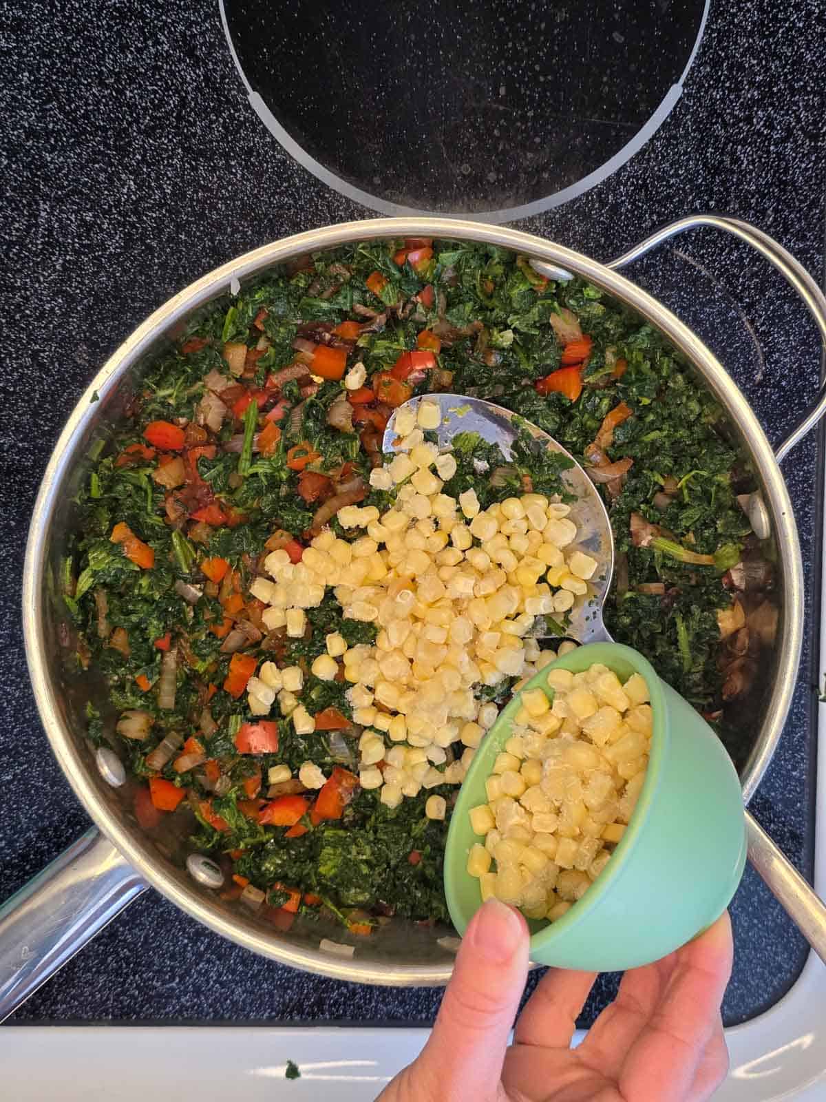 Corn being added to the skillet with black beans and seasoned vegetable filling.