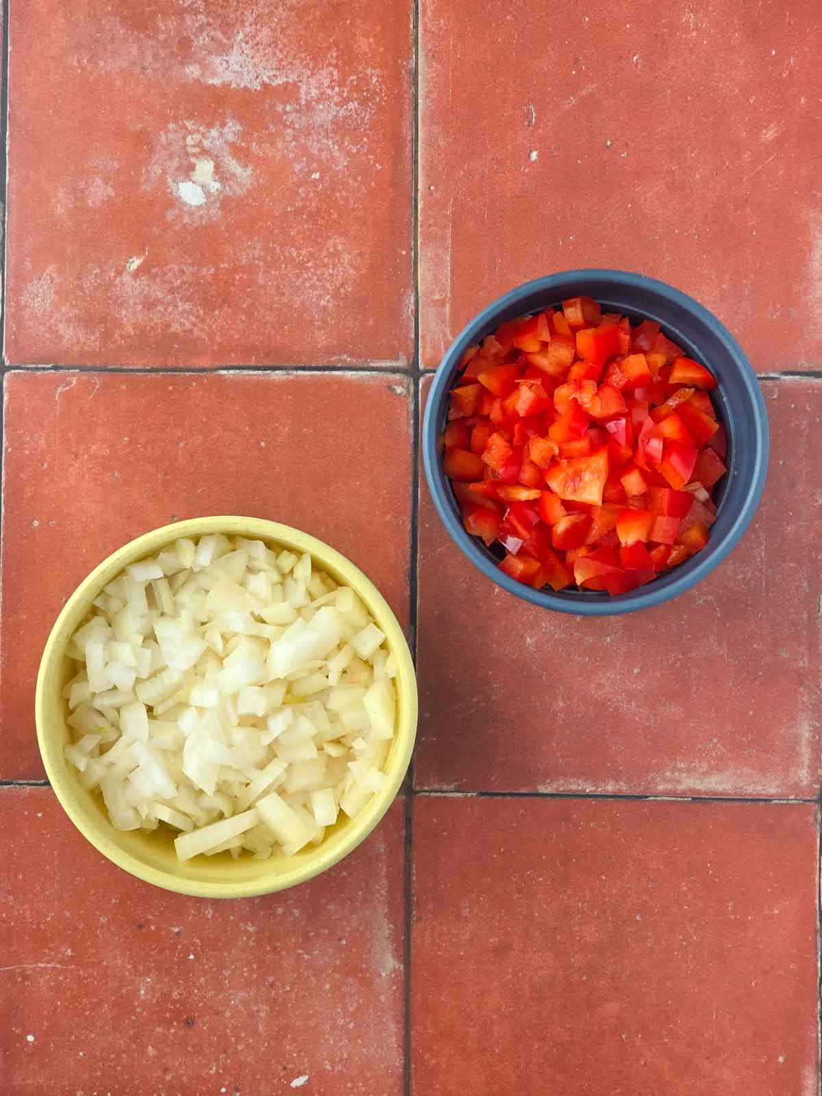 Bowls of diced onion and chopped red bell pepper prepared for cooking.