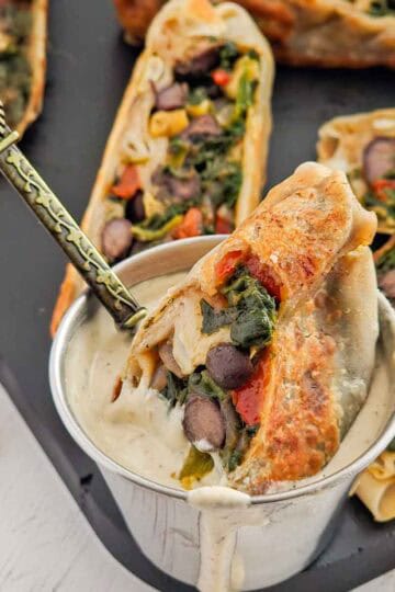 Crispy southwest egg roll dipped into creamy ranch dressing, showing the vegetable filling inside.