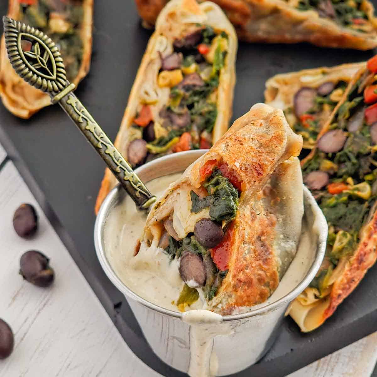 Crispy southwest egg roll dipped into creamy ranch dressing, showing the vegetable filling inside.