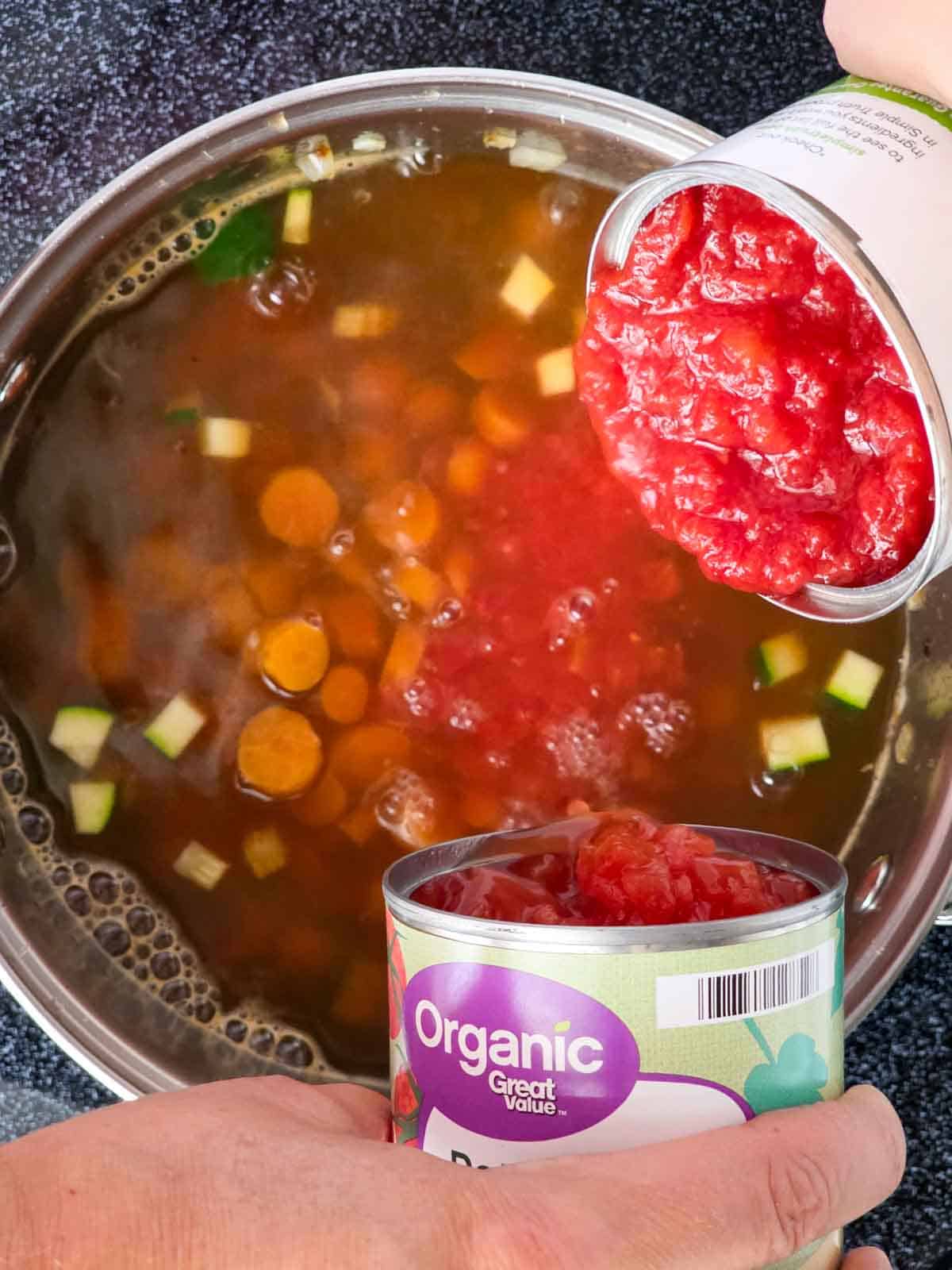 Canned crushed and diced tomatoes being poured into the soup pot.