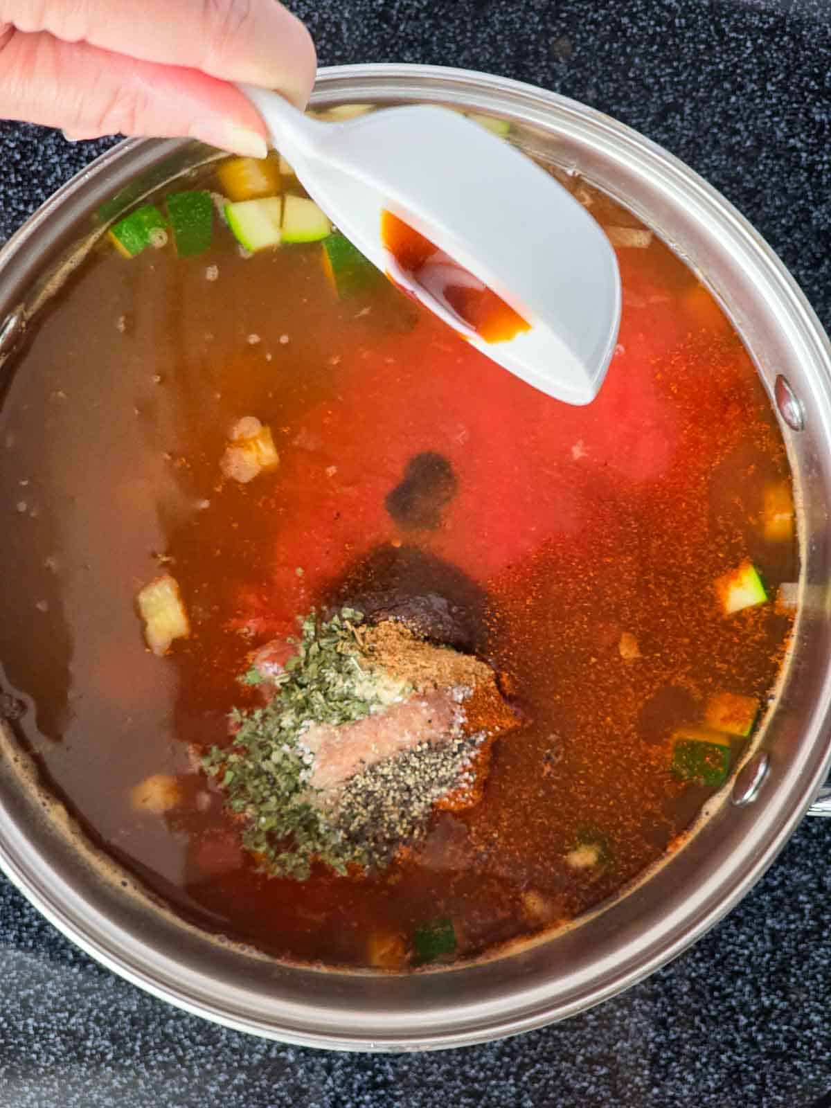 Vegan Worcestershire sauce being added to the soup pot.