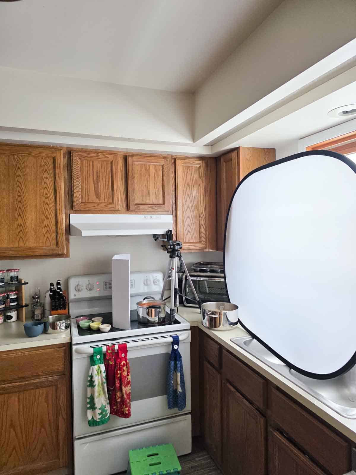 Home kitchen food photography setup with tripod, reflector, and soup pot staged for overhead shots.