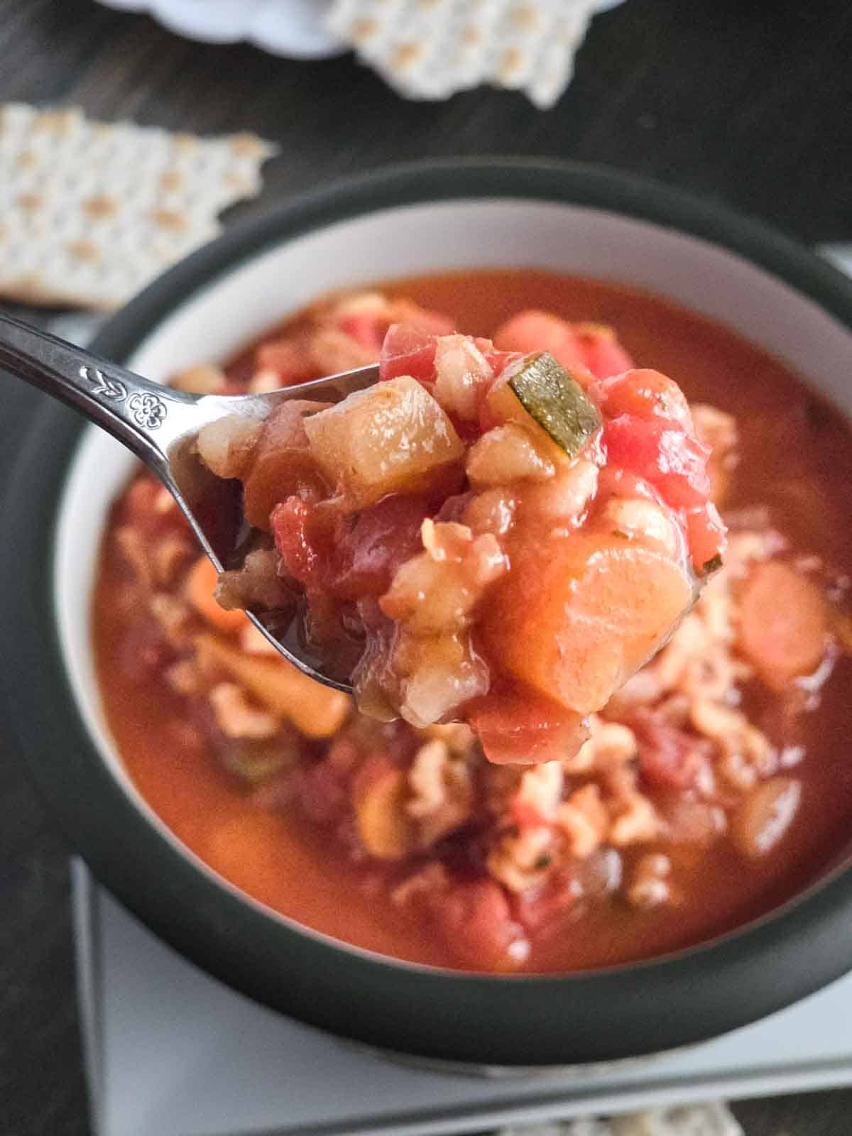 Close-up of vegetable barley soup in a bowl with a spoonful lifted, showing the chunky texture and vegetables.