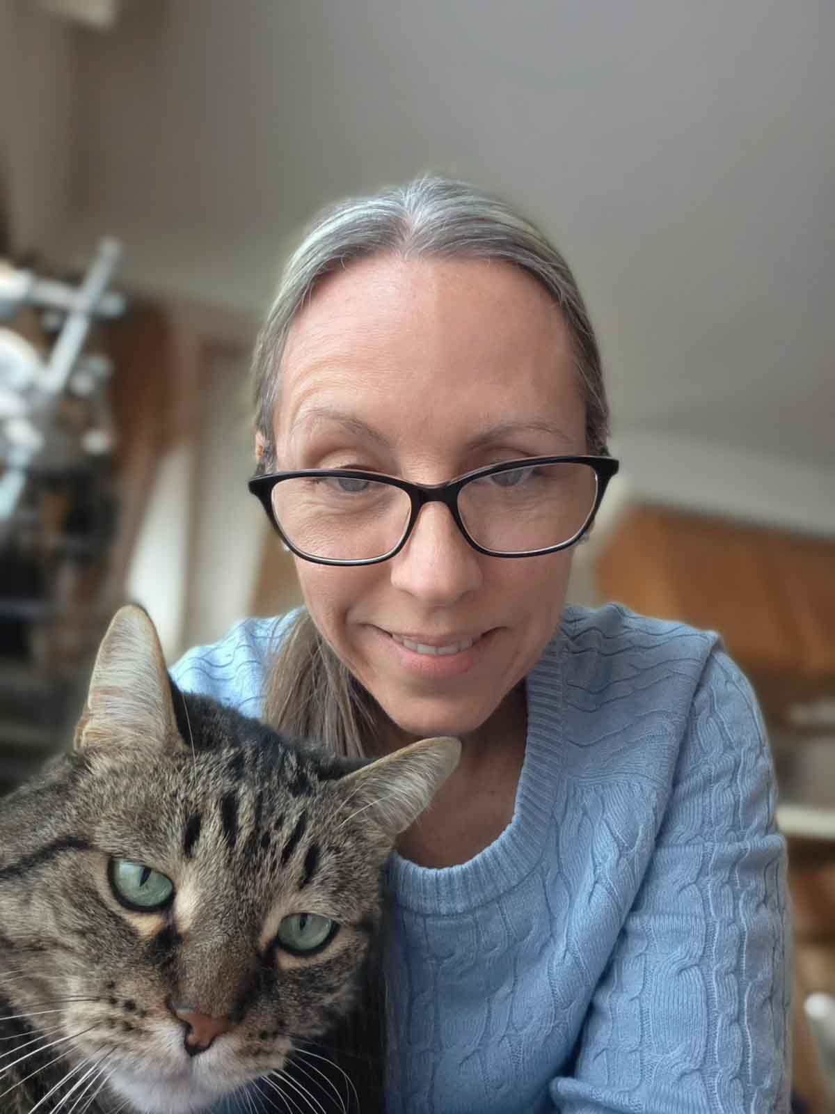 A tabby cat smugly looking at the camera with a woman behind him.