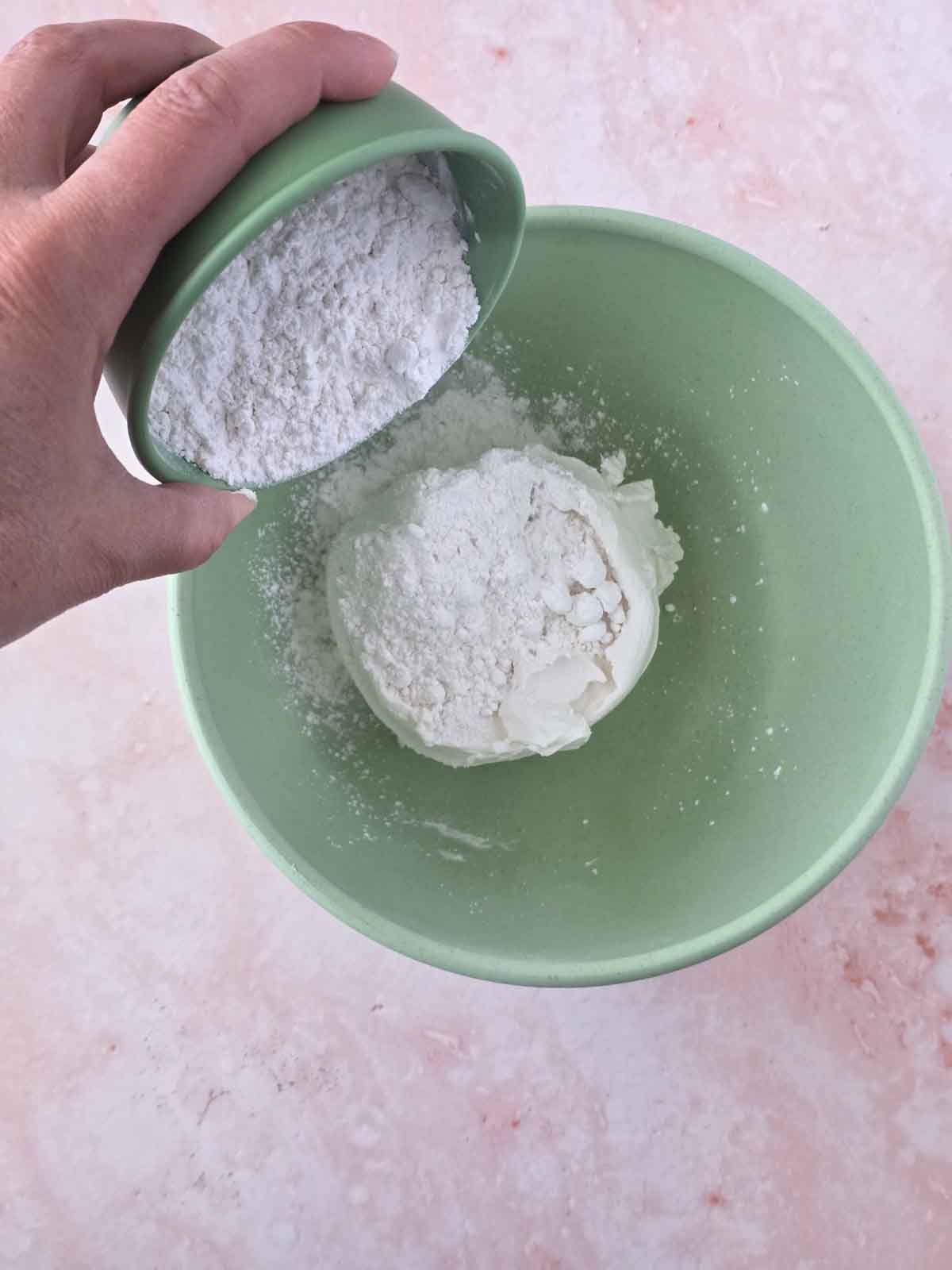 Adding powdered sugar to plant based cream cheese in mixing bowl.