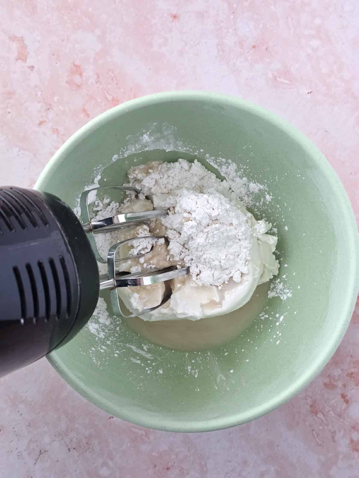 Hand mixer beating ingredients in bowl.