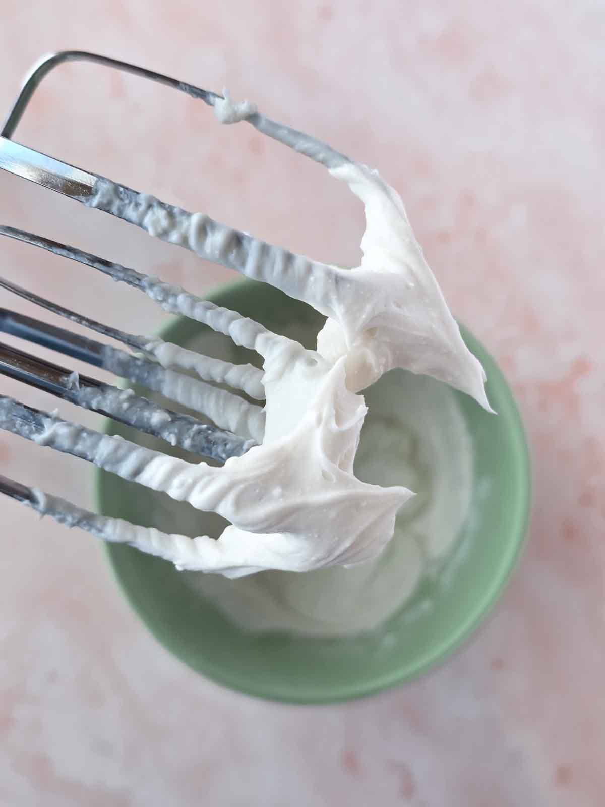 Vegan cream cheese frosting on mixer beaters showing thick, silky smooth texture.