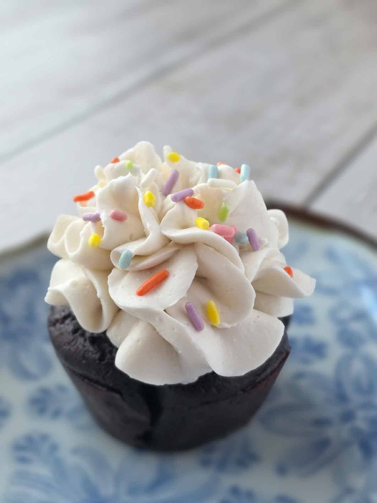 Vegan chocolate cupcake topped with piped vegan cream cheese frosting and rainbow sprinkles.