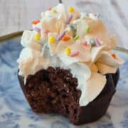 Chocolate cupcake with bite taken out showing moist crumb and cream cheese frosting.