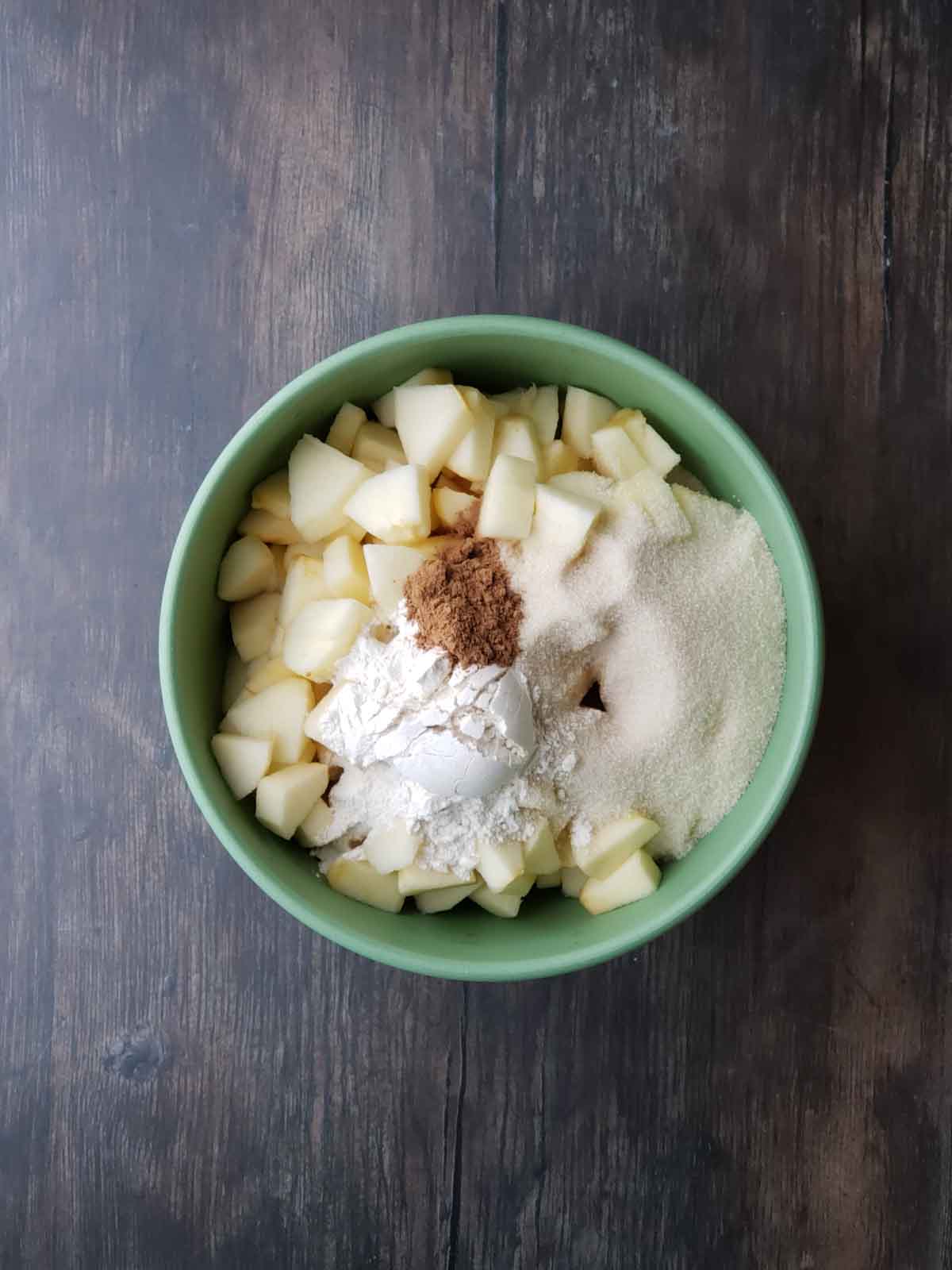 Chopped apples in a mixing bowl with flour, cinnamon, and sugar ready for combining.