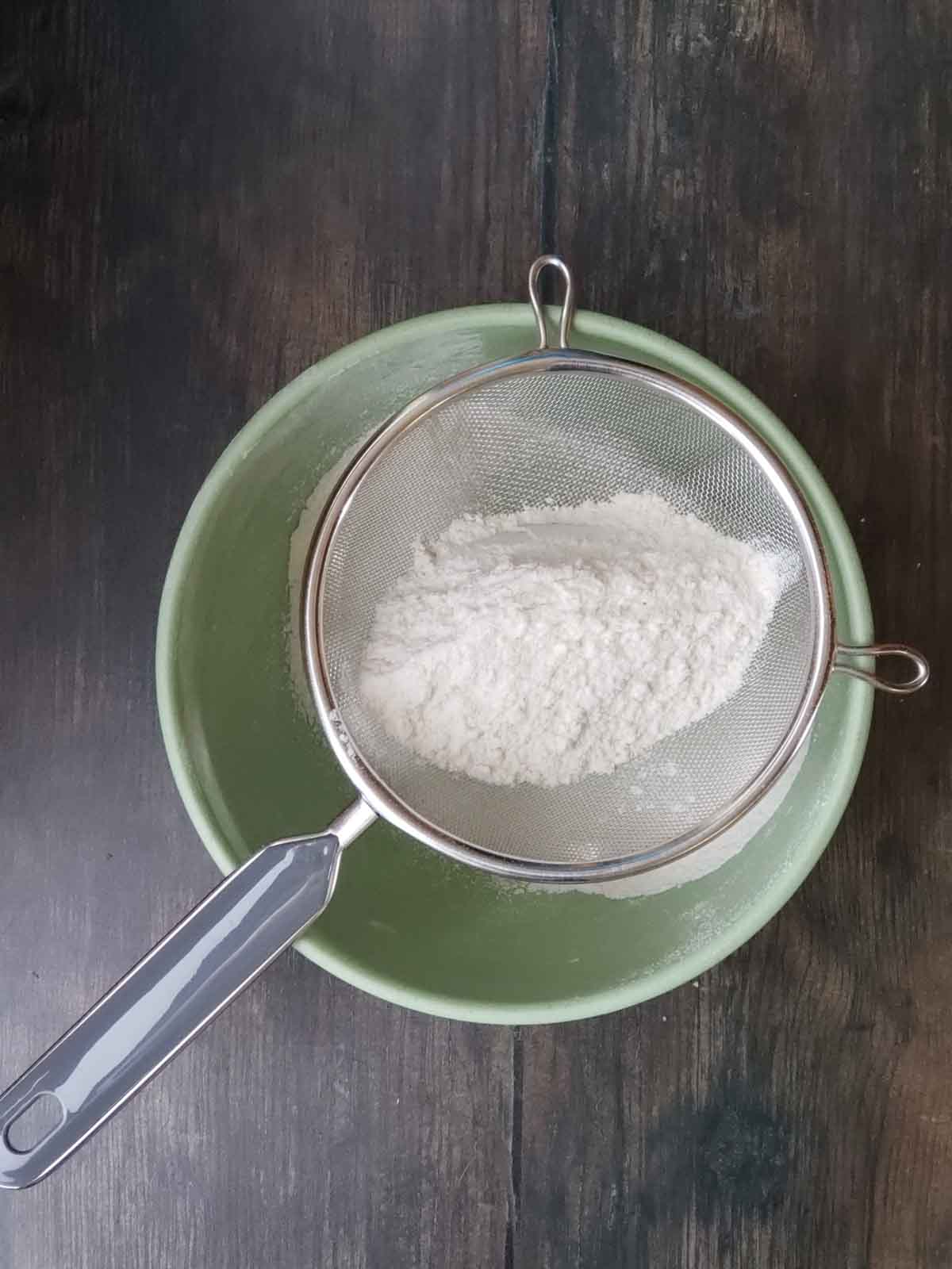 Flour shown in a sifter over a mixing bowl.