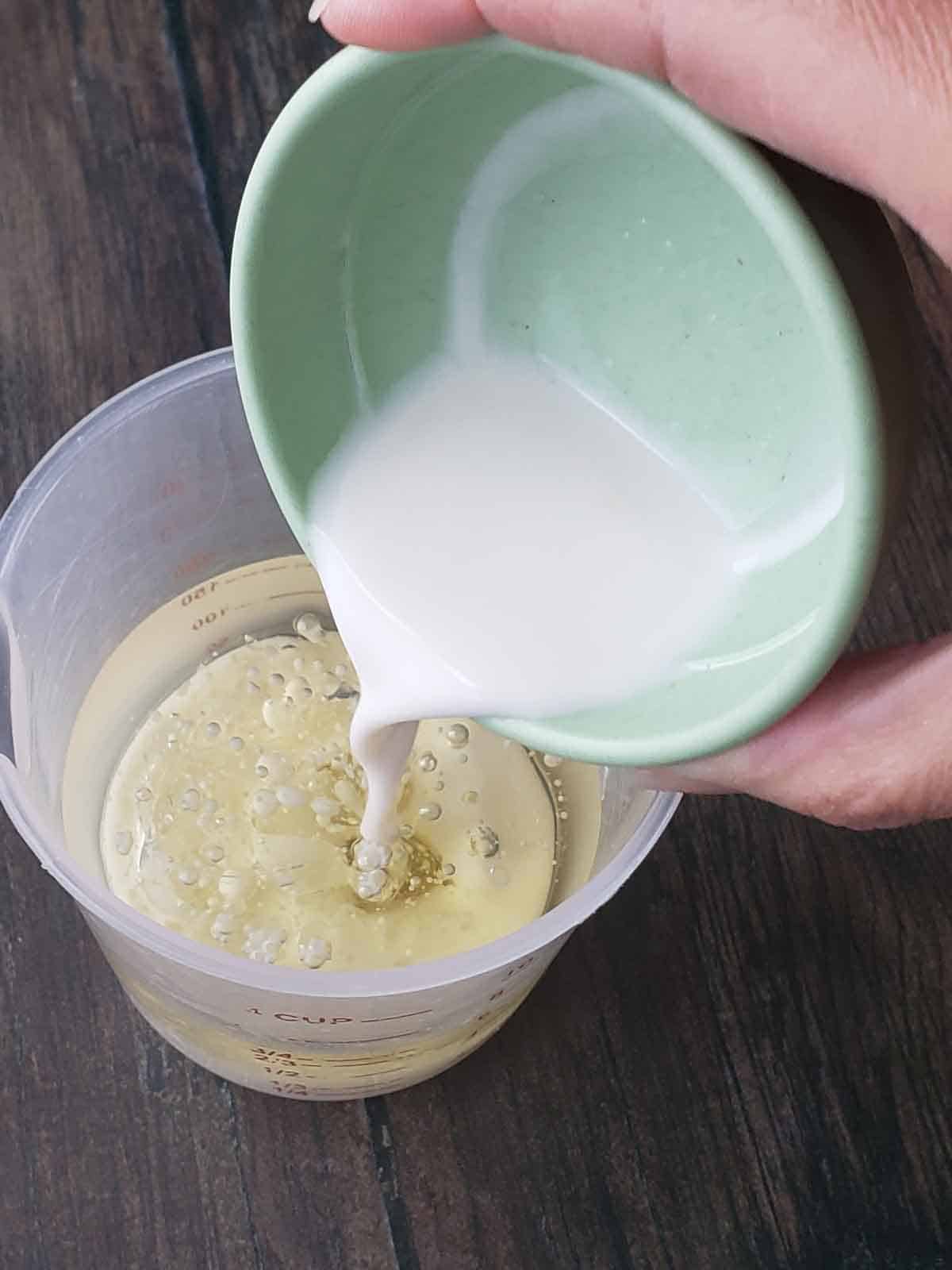 Plant milk being poured into a measuring cup with oil in it.