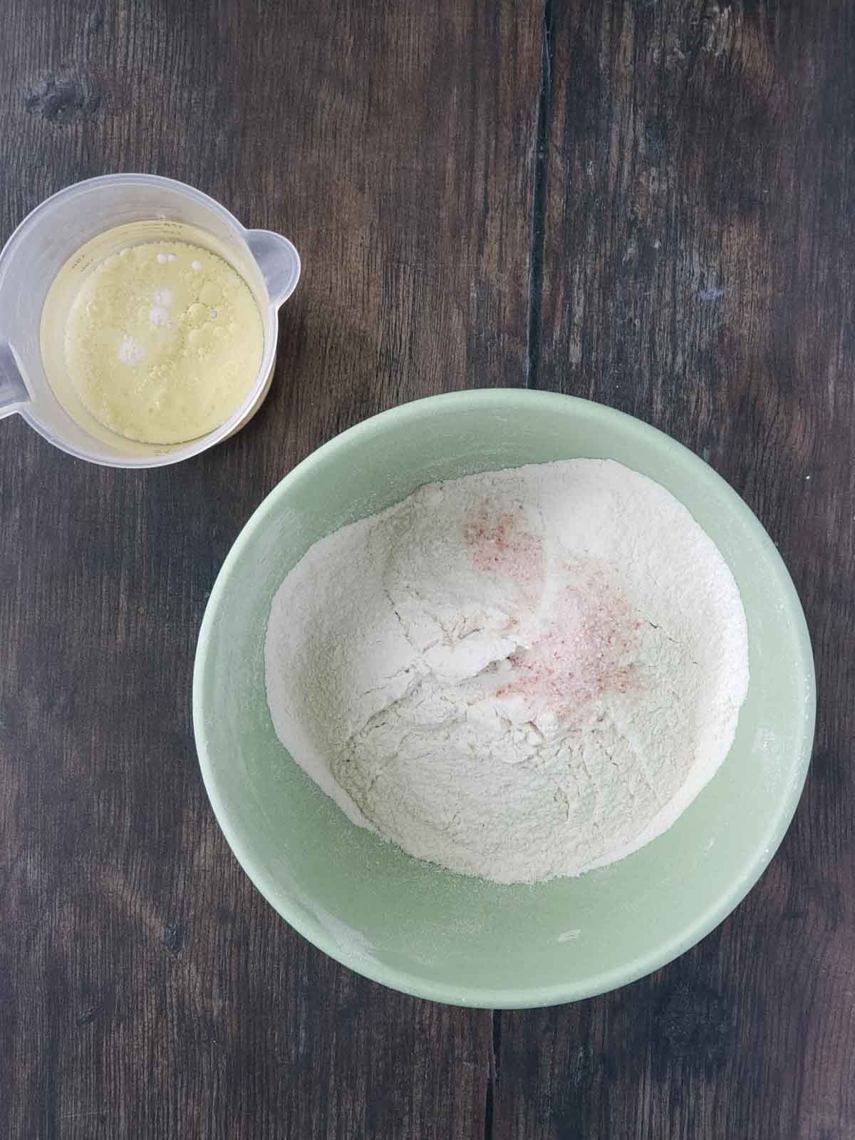 A measuring cup with milk and oil and a mixing bowl with dry ingredients to make the crust.