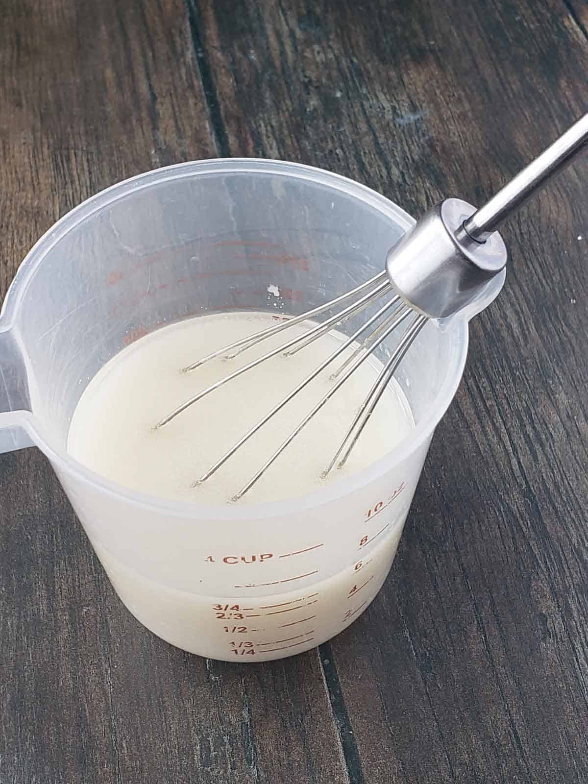 The milk and oil in a measuring cup being whisked together.