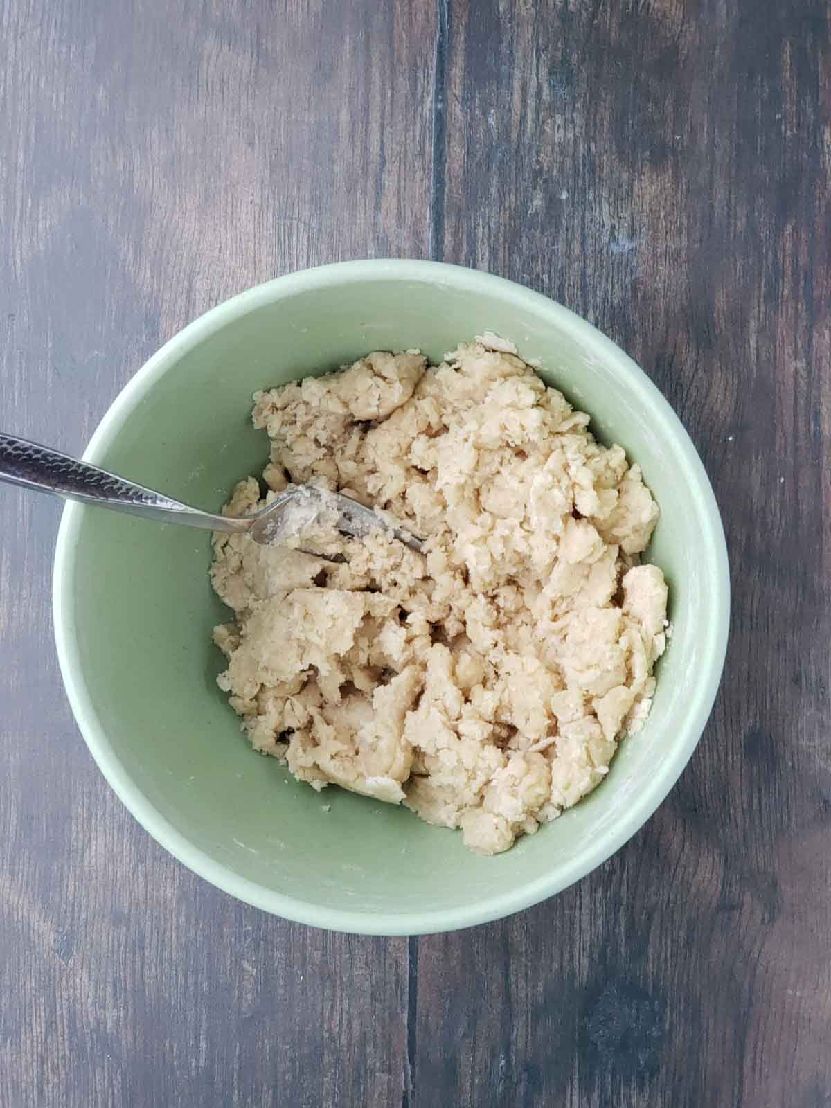 A fork being used to combine the dough ingredients in a medium green mixing bowl.