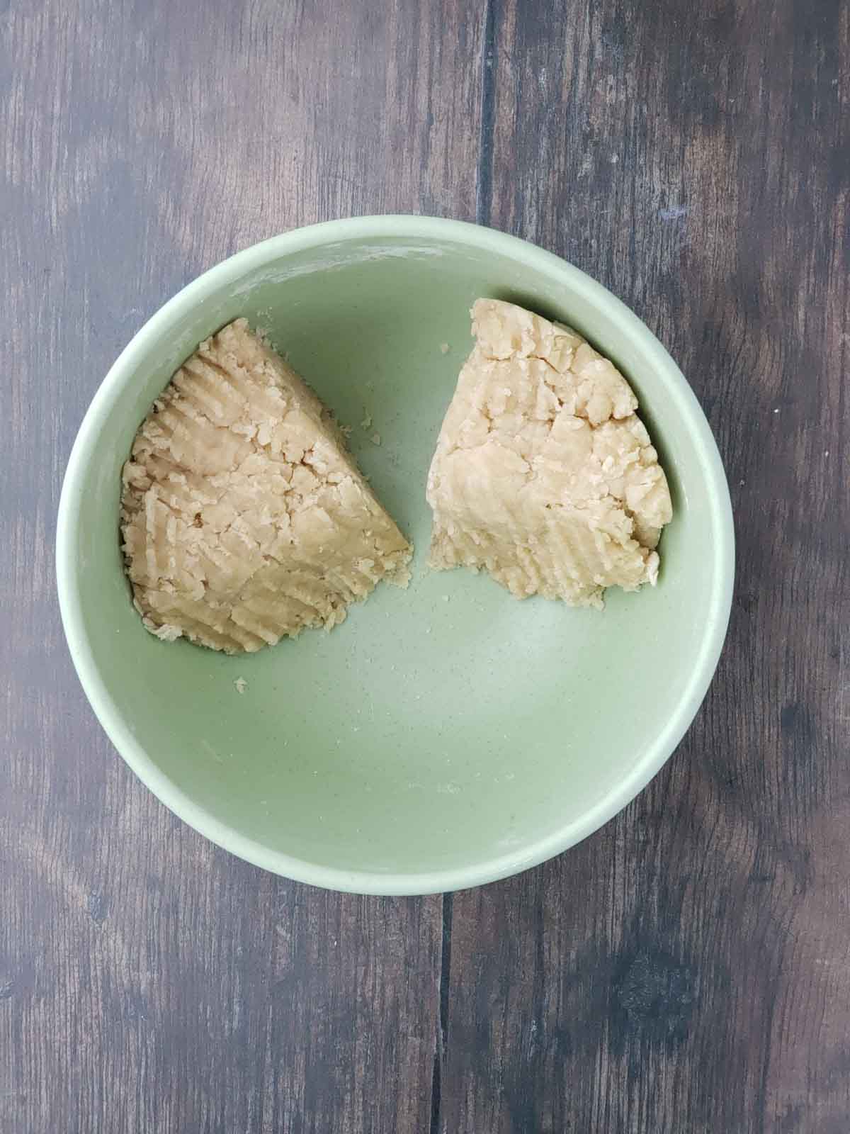 The dough for the apple pie crust shown divided in a green mixing bowl.