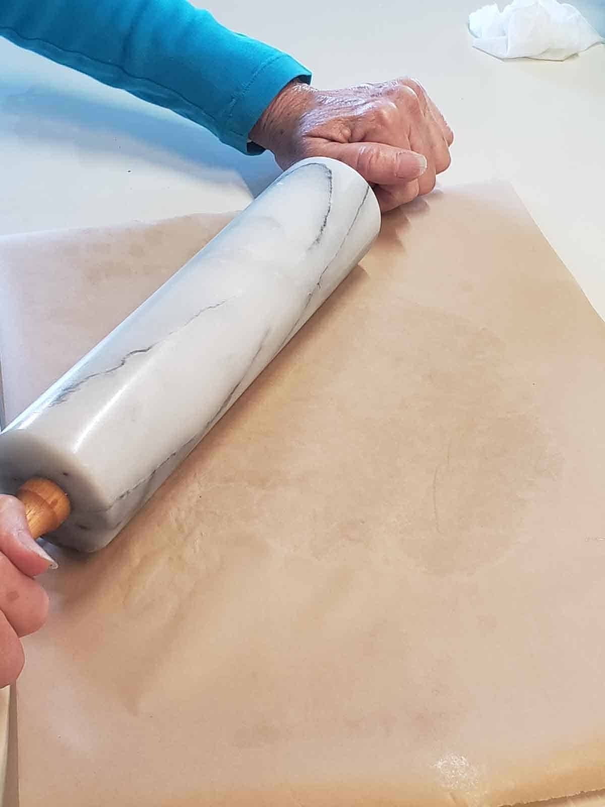 Hands shown rolling out the dough between two pieces of wax paper.