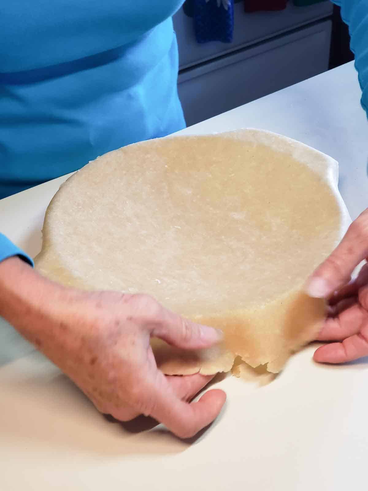 A pie crust shown draped over a pie dish ready for fitting.