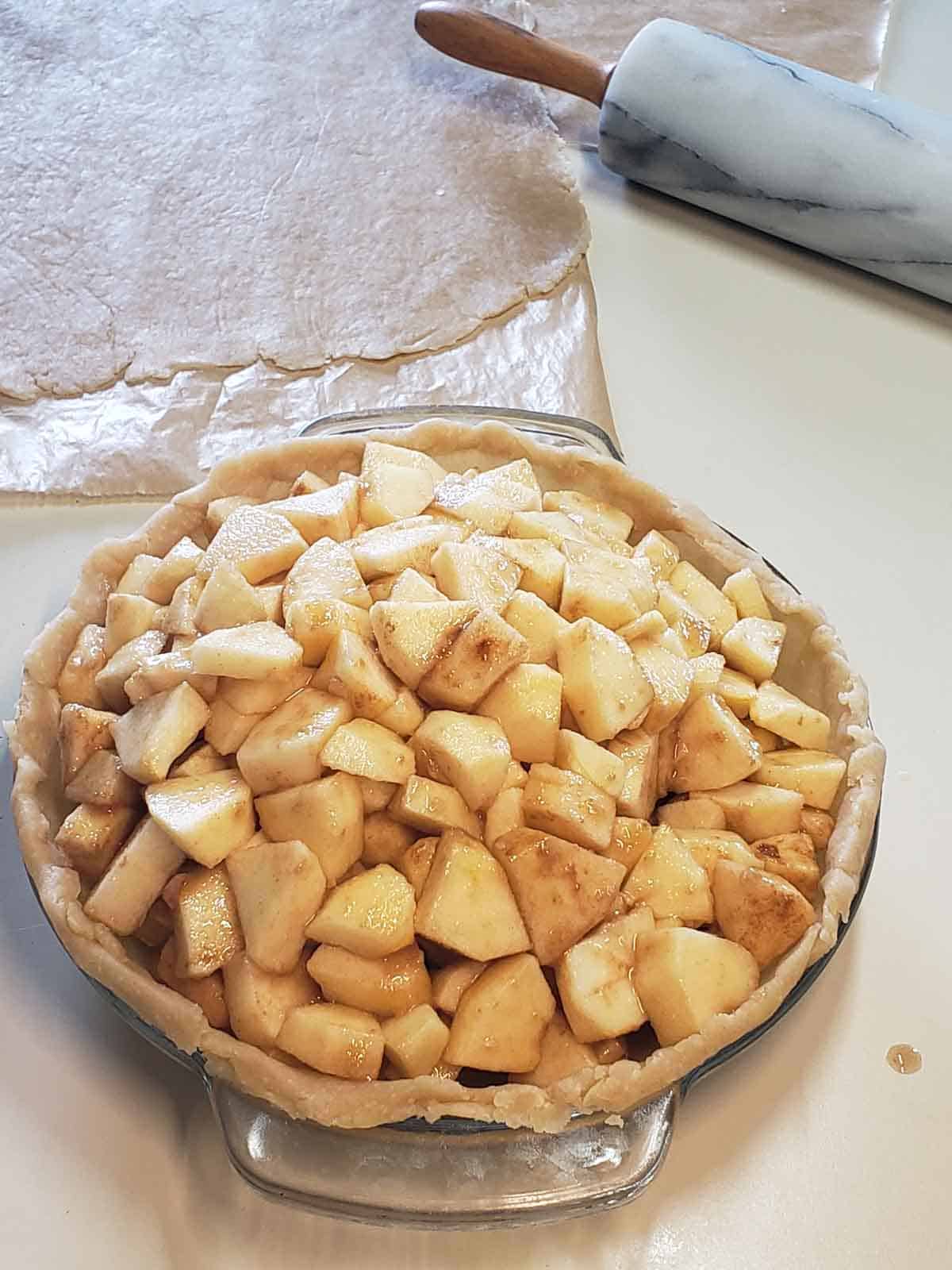 The pie shown with a heaping mound of cinnamon and sugar apples inside it before adding the top crust.