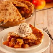 Slice of vegan apple pie with flaky crust and gooey cinnamon sugar apples topped with a scoop of dairy free vanilla ice cream.