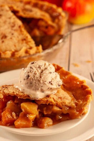 Slice of vegan apple pie with flaky crust and gooey cinnamon sugar apples topped with a scoop of dairy free vanilla ice cream.
