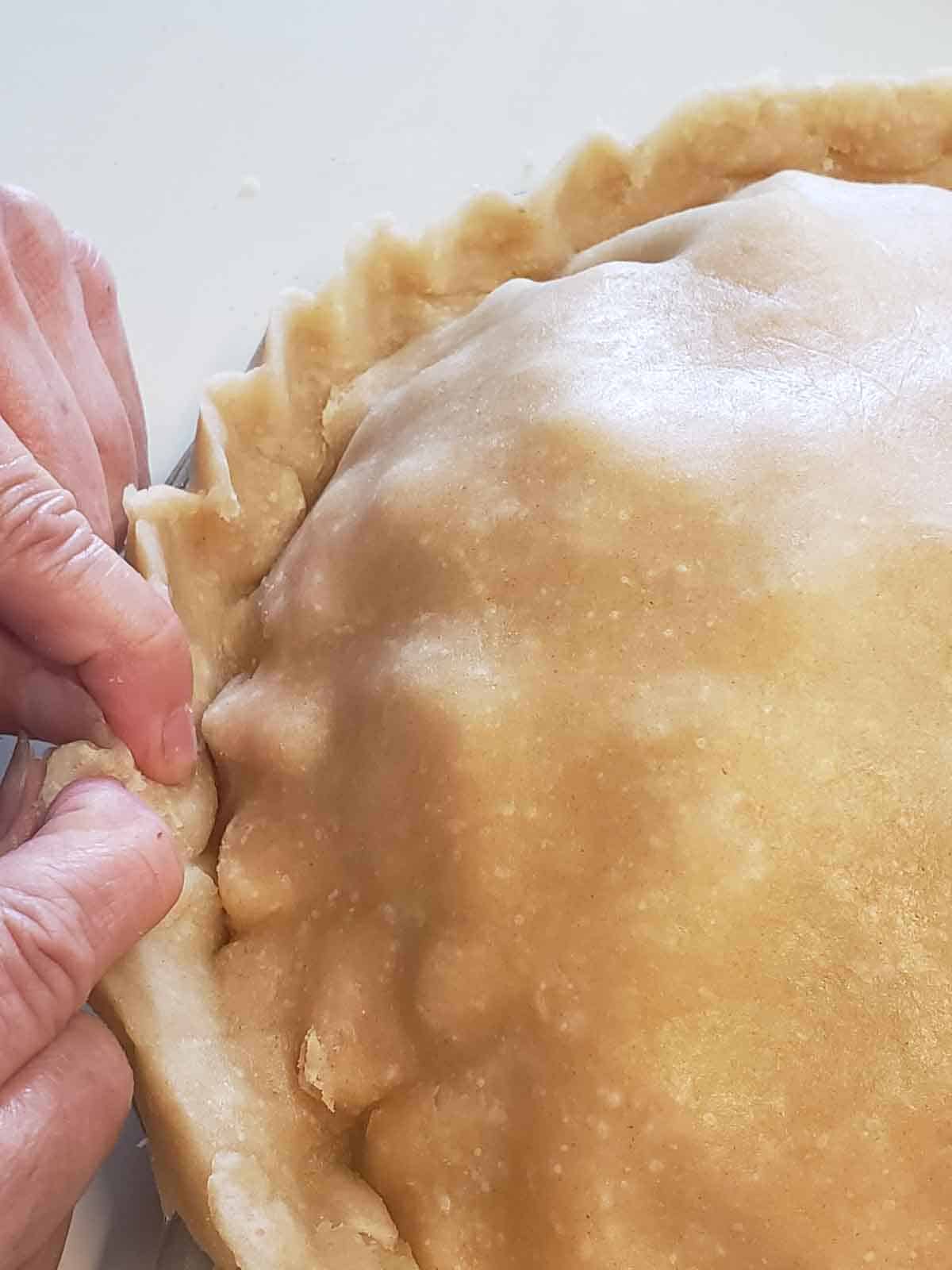 A hand shown pinching the crust to seal the edges.
