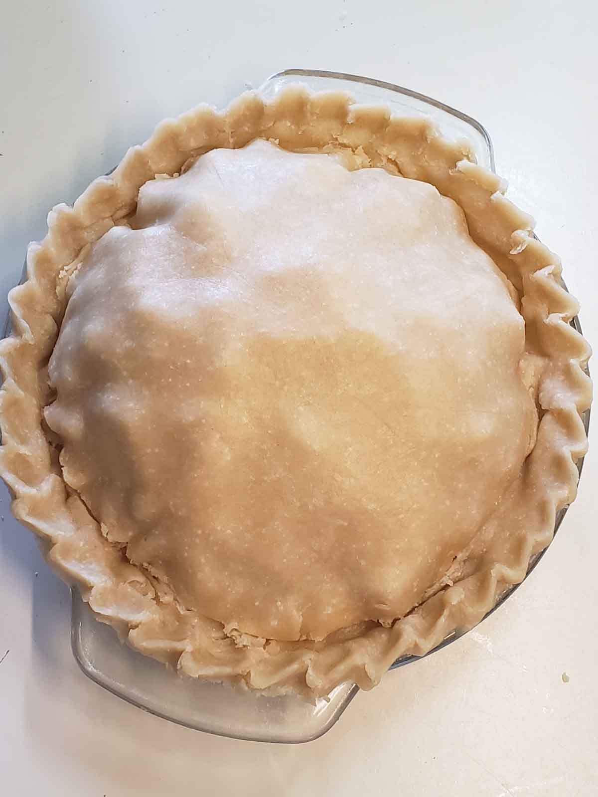 An unbaked pie shown with knife cuts made around the edges for venting while baking.