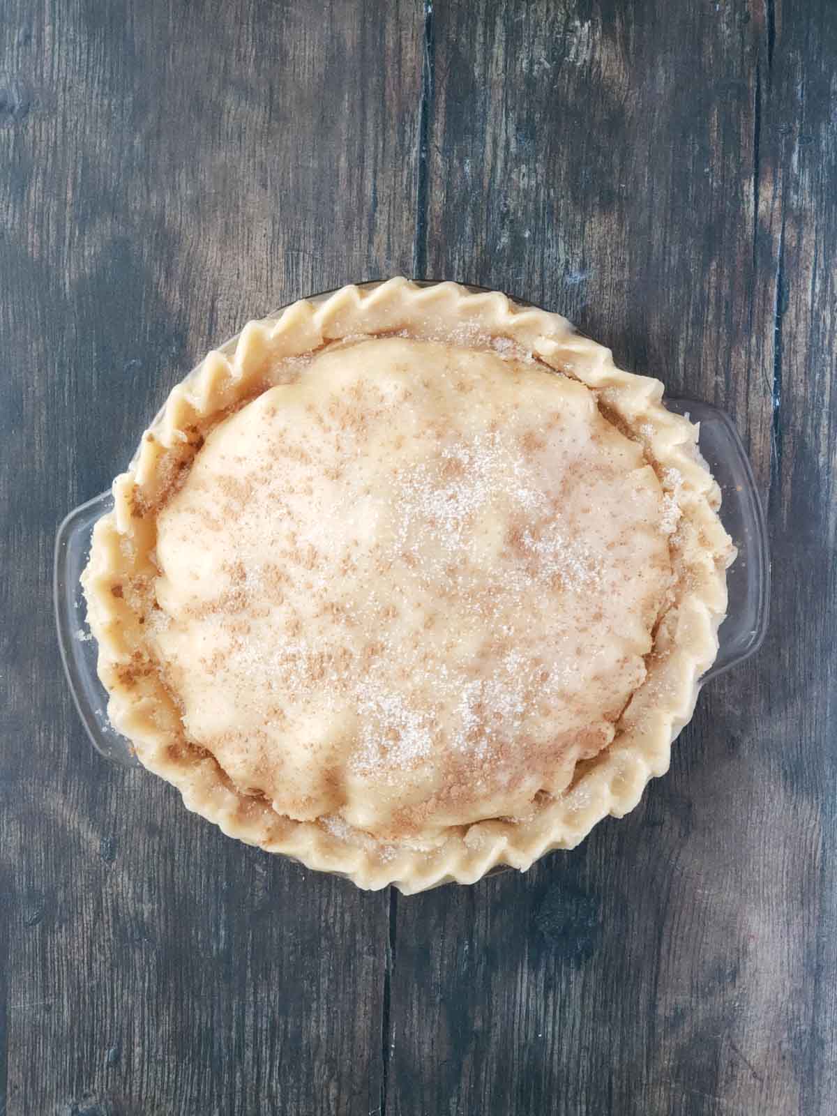 Overhead of unbaked apple pie sprinkled with cinnamon and sugar ready for baking.