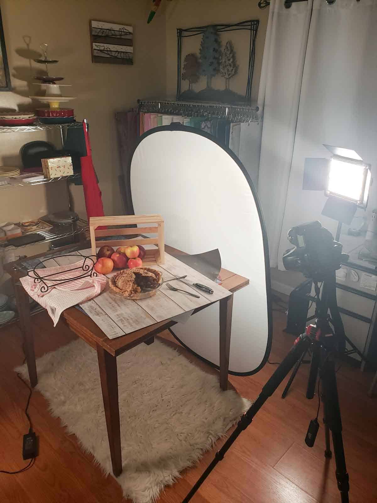 Studio set up for apple pie photoshoot showing pie on a table with apples and other props.