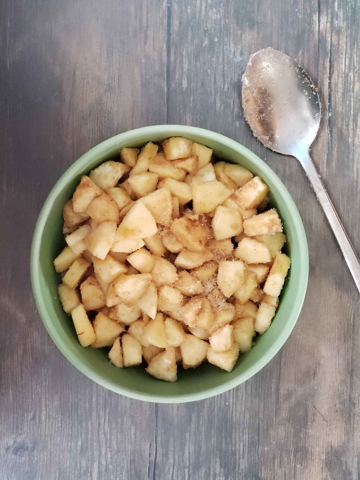 Chopped apples coated with cinnamon and sugar in a mixing bowl with a large spoon.
