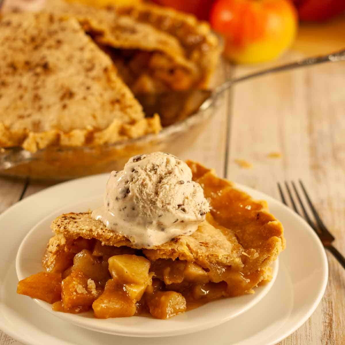 Slice of vegan apple pie with flaky crust and gooey cinnamon sugar apples topped with a scoop of dairy free vanilla ice cream.