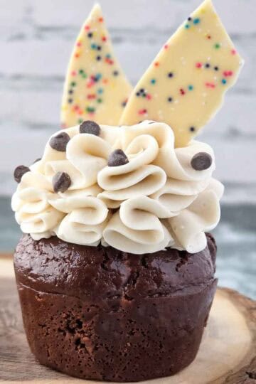 Decorated chocolate cupcake with cream cheese frosting, mini chocolate chips, and white chocolate pieces.