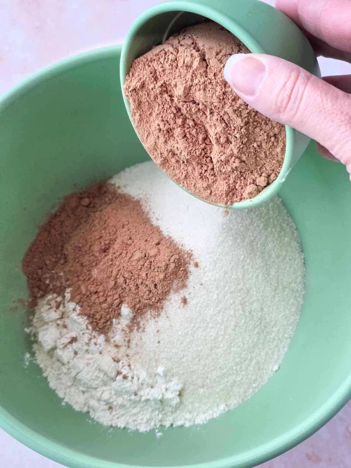 Cocoa powder being added to the dry ingredients in a mixing bowl.