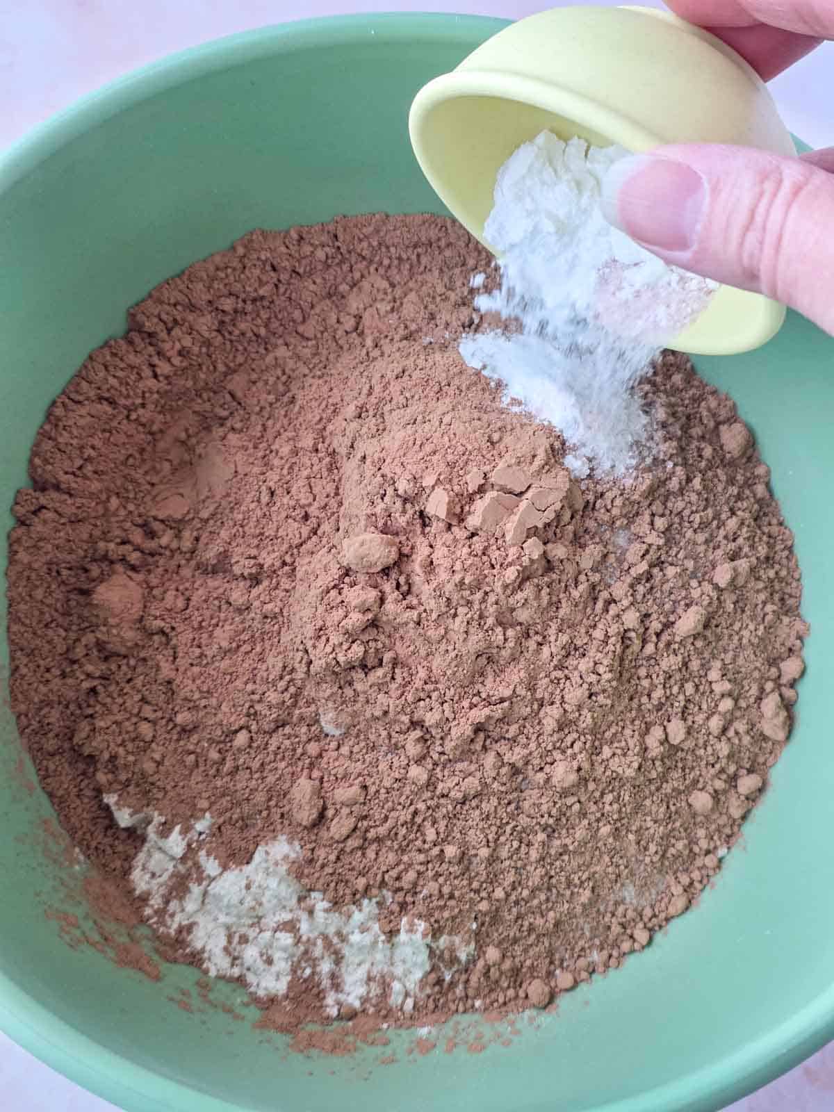 Baking powder being sprinkled over cocoa and flour mixture for chocolate cupcake batter.