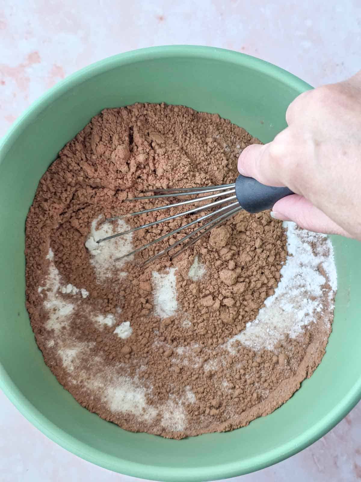 Whisk mixing dry ingredients together in a green bowl before adding wet ingredients.