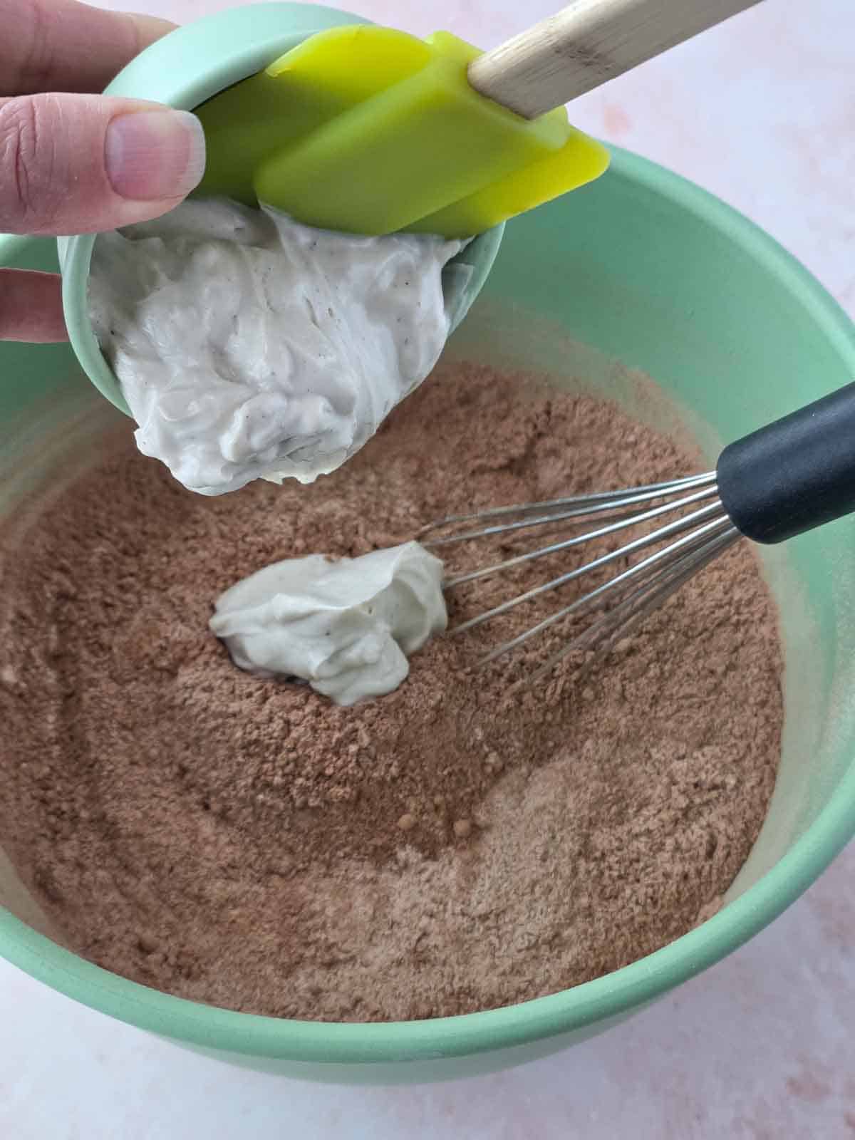 Vanilla dairy-free yogurt being added to the bowl of dry ingredients.